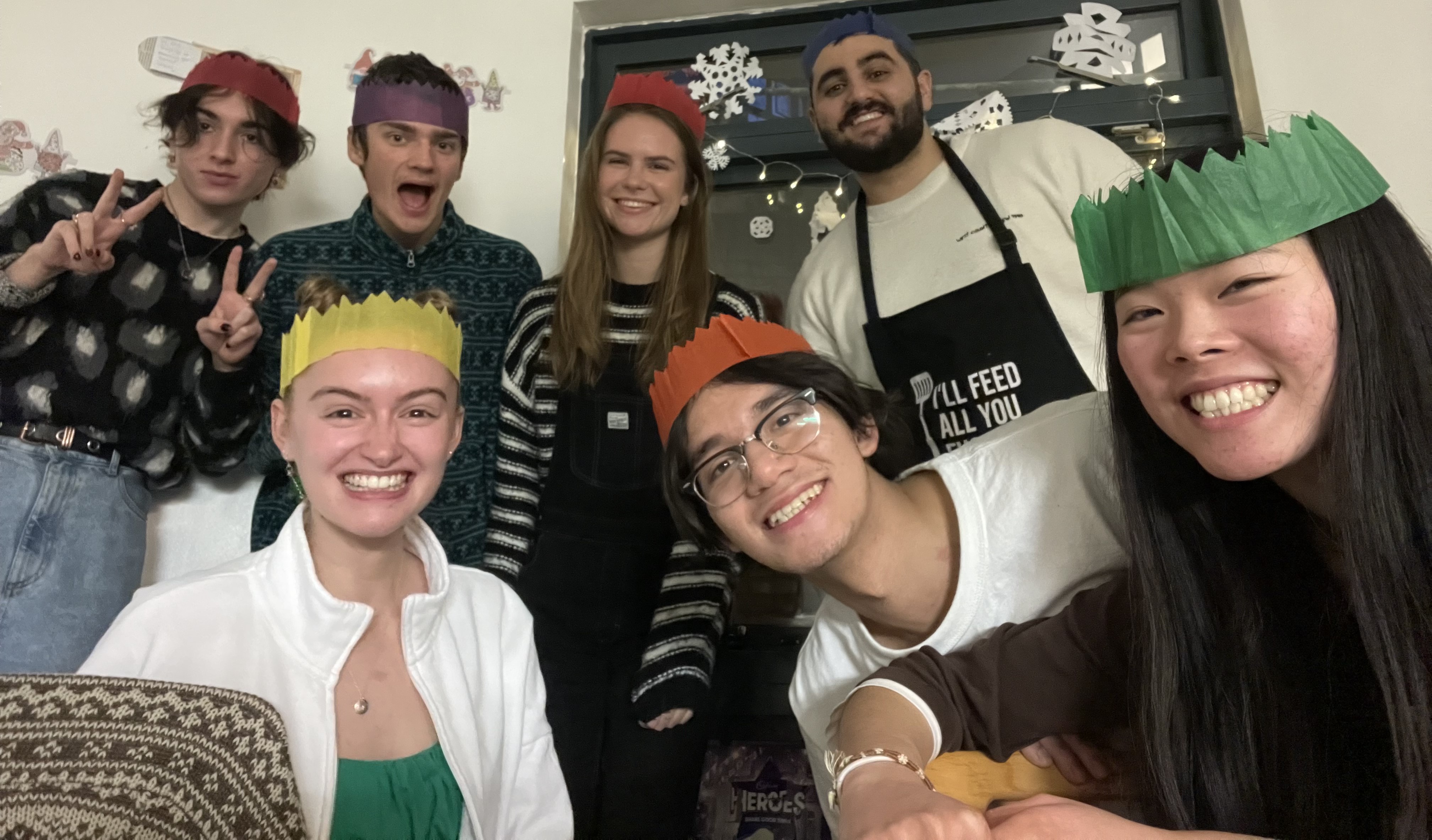 7 people grinning at the camera with various coloured tissue paper Christmas cracker hats on