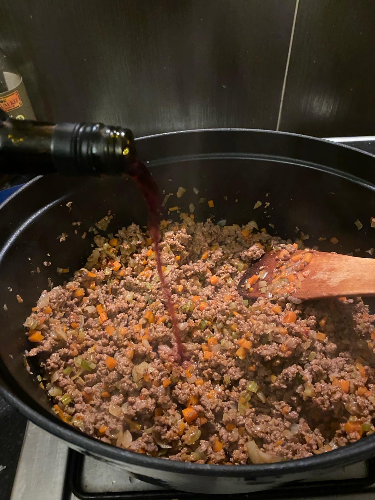 Photo of red wine being poured into a pot of bolognese.